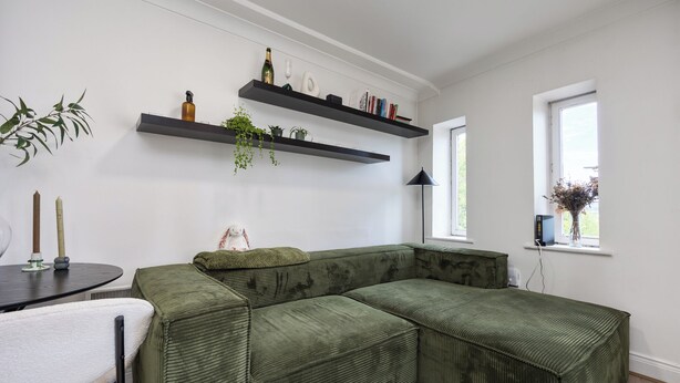 Un sofá seccional verde, una mesita redonda pequeña con una silla blanca y una mesa de centro de vidrio.