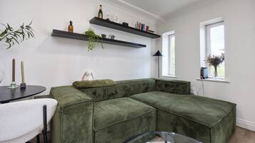 A green sectional sofa, a small round table with a white chair, and a glass coffee table.