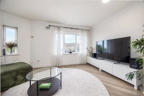 Uma sala de estar moderna com televisão de tela plana, mesa de centro de vidro, sofá verde e radiador branco.