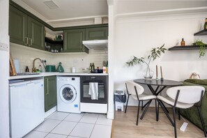Uma cozinha compacta com máquina de lavar, forno e área de refeições com cadeiras e mesa.