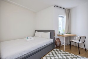 A neatly made bed with white linens, a desk with a chair, and a window with curtains. - Central 2BR Flat w/balcony Near Temple Bar (The Liberties)