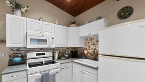 Una cucina con mobili bianchi, un forno a microonde, un fornello e un frigorifero.