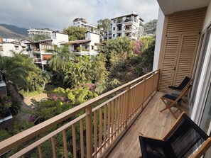 A balcony with wooden railings, two chairs, and a view of a residential area with houses and greenery. - Luxury 2B Romantic Zone Condo , Rooftop Pool, 2-Min Walk to Beach (Puerto Vallarta)