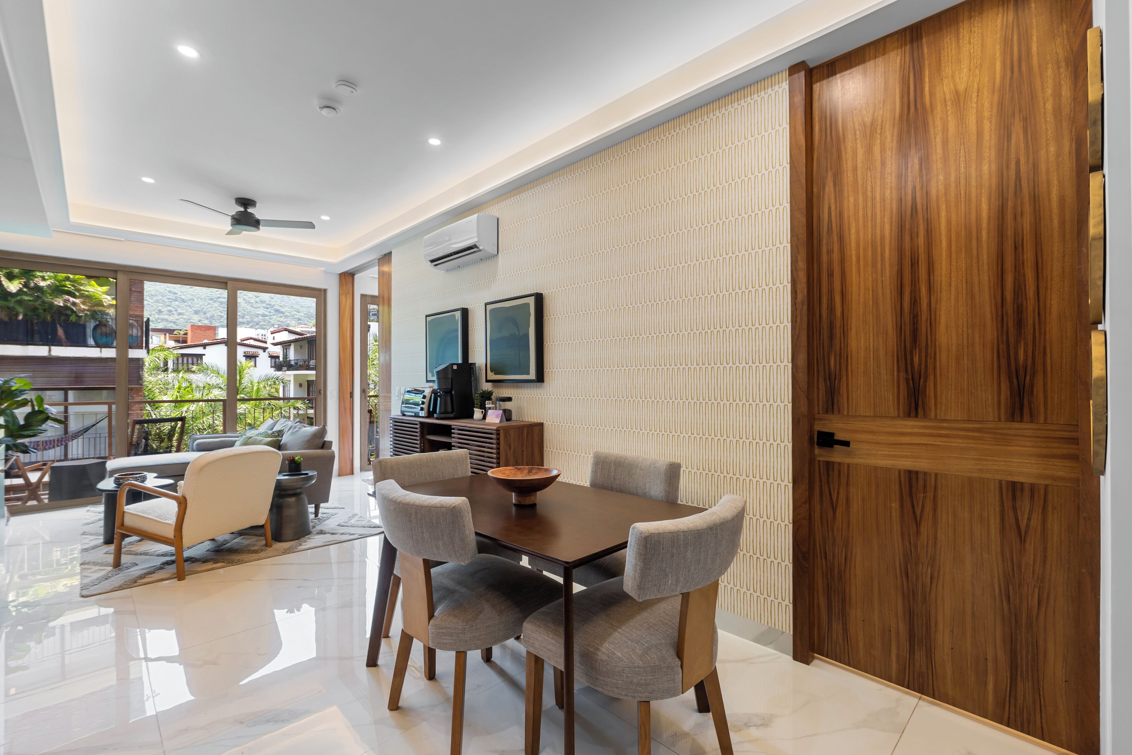 A modern dining area with a wooden table and chairs, a patterned wall, and a view of the outdoors.