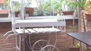 Ein Sitzbereich im Freien aus Metall mit Tisch und Stühlen, umgeben von Topfpflanzen und einer Backsteinmauer.