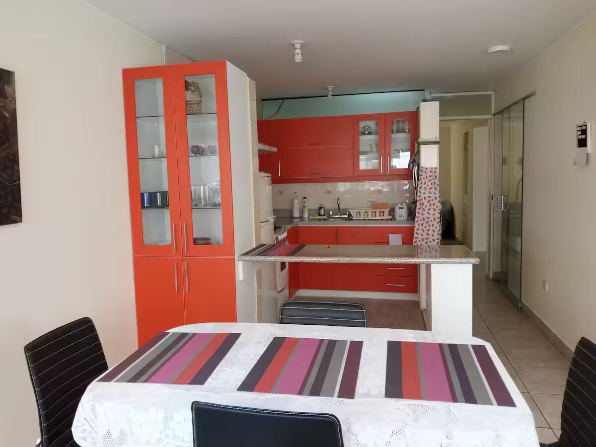 Une cuisine compacte avec des meubles de rangement rouges, un îlot central et un coin repas comprenant une table et des chaises.