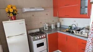 Eine kleine Küche mit Kühlschrank, Herd, Backofen und roten Schränken.