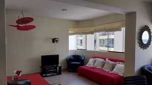 Ein Wohnzimmer mit einem roten Sofa, einem schwarzen Sessel, einem Fernseher und einem Esstisch.
