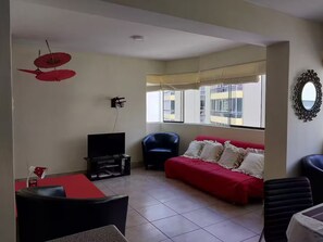 Una sala de estar con un sofá rojo, una silla negra, un televisor y una mesa de comedor.