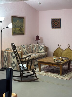 A living room with a patterned sofa, a rocking chair, a coffee table, and a lamp.