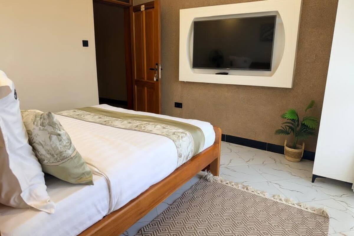 Un dormitorio con cama, televisor montado en la pared, una puerta y una planta en maceta.