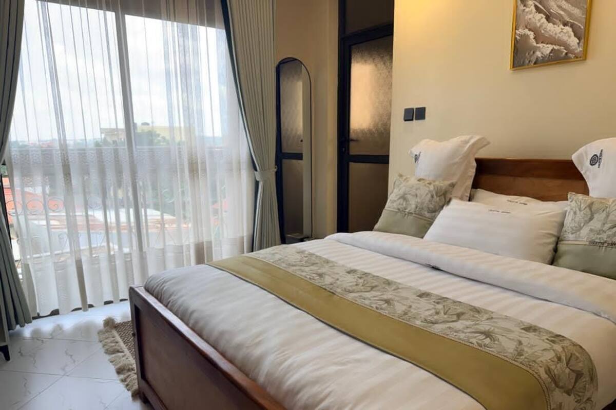 Habitación de hotel con cama, cortinas, vistas por la ventana y un cuadro en la pared.