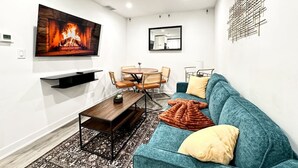 En moderne stue med pejs, spisebord med stole, sofa med hynder og et ophængt kunstværk.