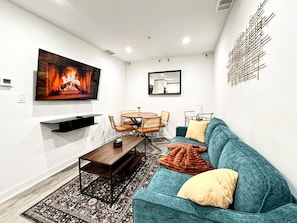 Ein modernes Wohnzimmer mit Kamin, Esstisch mit Stühlen, einer Couch mit Kissen und einem Wandbild.