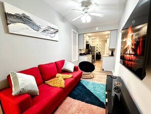 A living room with a red sofa, a black chair, a TV, and a ceiling fan. - Cozy and Charming Forest Park Apt with Parking - Easy Access to City + Airports (Forest Park)