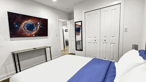 Hotellihuone, jossa on suuri sänky, työpöytä, peili ja galaksiteemalla koristeltu seinätaulu.