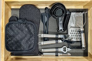 A drawer containing a black quilted bag, black utensils, a grater, a metal bottle opener, and a metal can opener. - Galactic Getaway - 15 Min to Midway - Easy Access to Chicago (Berwyn)