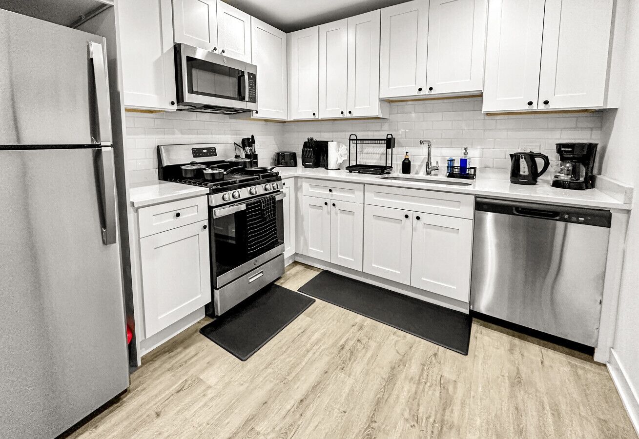 A modern kitchen with white cabinets, stainless steel appliances, and a wood floor.