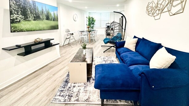 Un salon moderne avec un canapé bleu, un téléviseur à écran plat, un coin repas avec des chaises et un fauteuil suspendu.