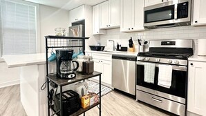 Une cuisine moderne avec des meubles blancs, des appareils en acier inoxydable, un coin café et un plancher en bois.