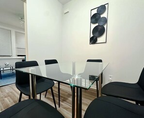 Ein moderner Besprechungsraum mit Glastisch, schwarzen Stühlen und einem schlichten Wandbild.