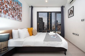 Ein modernes Hotelzimmer mit einem großen Bett, Blick auf die Stadt, einem Gemälde an der Wand und einem gerahmten Bild.