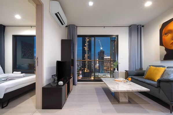 Ein modernes Hotelzimmer mit einem Bett, einer Couch, einem Couchtisch und einem großen Fenster mit Blick auf die Stadt.