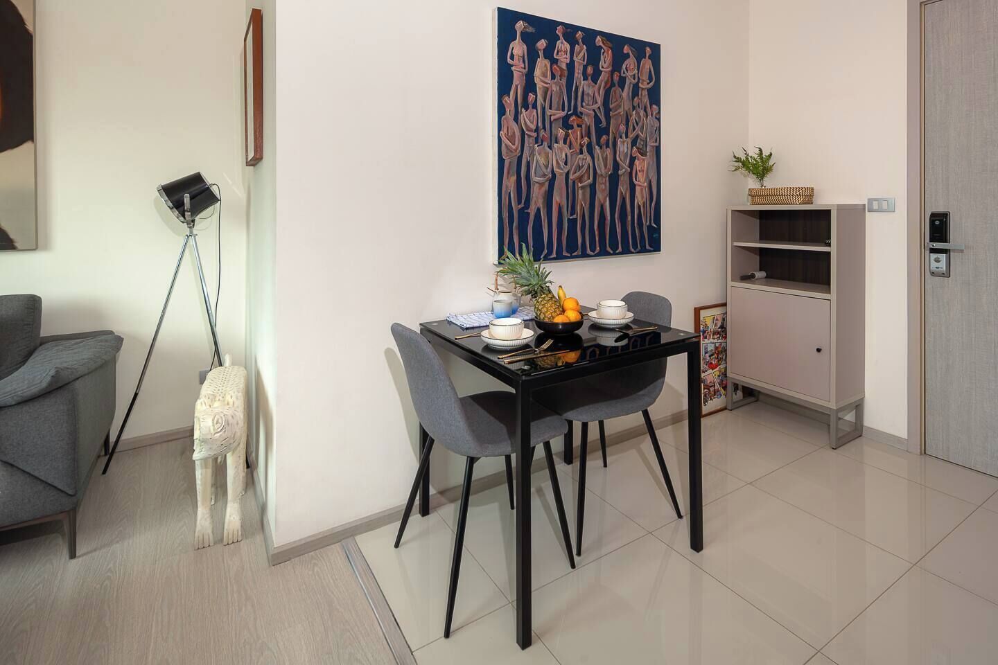 Een moderne woonkamer met een eettafel, stoelen, een lamp, een schilderij en een kast.