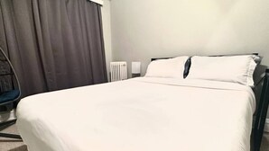 Una habitación de hotel con una cama, una silla, un radiador y una cortina.