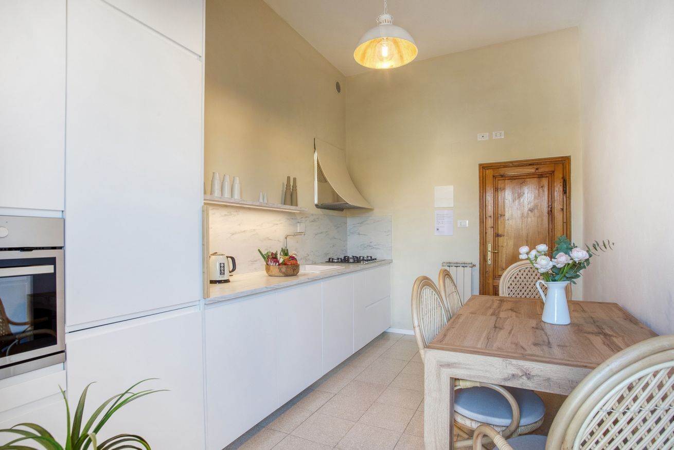 Une cuisine moderne avec des meubles blancs, une table à manger en bois et un luminaire suspendu.