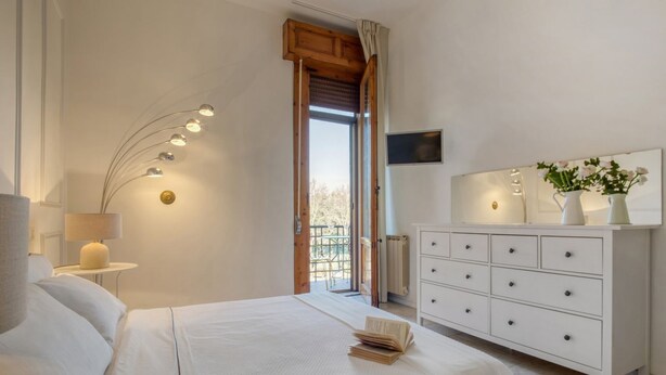 Een slaapkamer met een bed, bedlampje, dressoir en een televisie aan de muur.