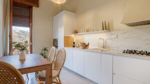 Een keuken met witte kasten, een marmeren aanrecht, een gasfornuis en een eethoek met rieten stoelen en een tafel.