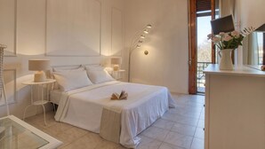 Een slaapkamer met een bed, nachtkastjes, een lamp, een vaas met bloemen en uitzicht door een raam.