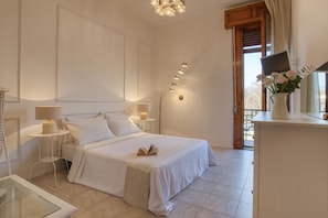 Ein Schlafzimmer mit einem Bett, Nachttischen, einer Lampe, einer Vase mit Blumen und Blick durch ein Fenster.