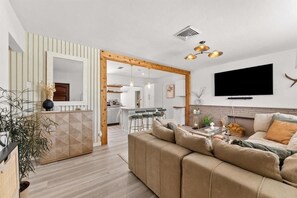 Ein modernes Wohnzimmer mit einer Couch, einem Fernseher und einer Küche im Hintergrund.