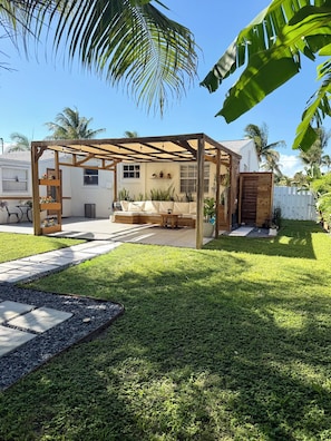 Ein überdachter Patio-Bereich mit einer Couch, einem Holztisch und einem Weg zum Haus.