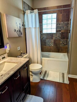 A bathroom with a toilet, sink, vanity, bathtub, shower curtain, and a window. - Fabulous  2-bedroom house near Downtown San Antonio! (San Antonio)