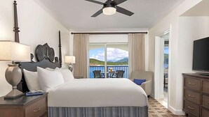 Een hotelkamer met een groot bed, een plafondventilator, een televisie, een bureau met een lamp en uitzicht op het omliggende landschap.