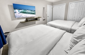 Ein Hotelzimmer mit zwei Betten, einem an der Wand befestigten Fernseher, einem Spiegel und weißen Türen.