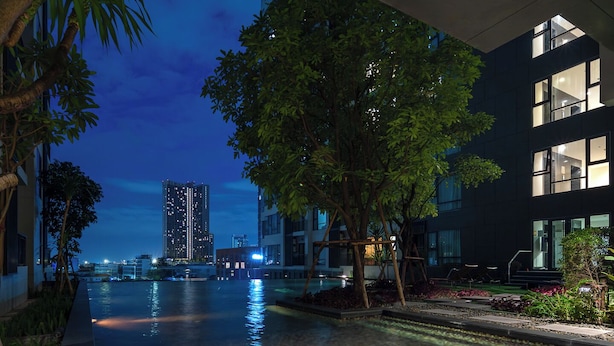 Un bâtiment moderne doté d’une piscine, entouré d’arbres et illuminé par le ciel nocturne.