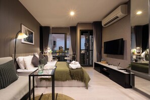 A modern hotel room with a bed, sofa, TV, and a desk with a lamp. - 5 Min to Metro, Washer & Dryer, Essentials, Gym (Khet Khlong Toei)
