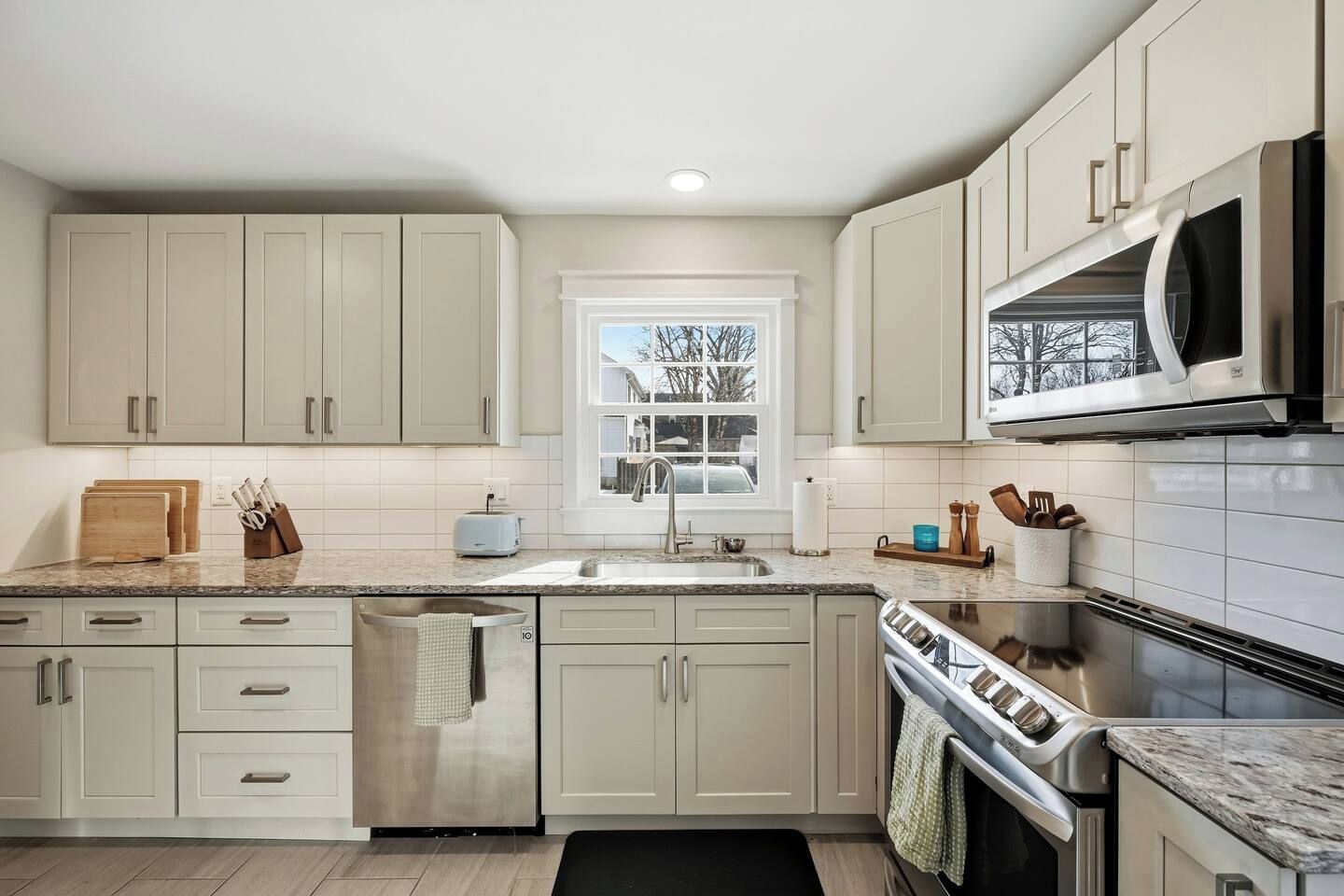 A modern kitchen with light-colored cabinets, a stainless steel sink, a built-in microwave, and a stove.