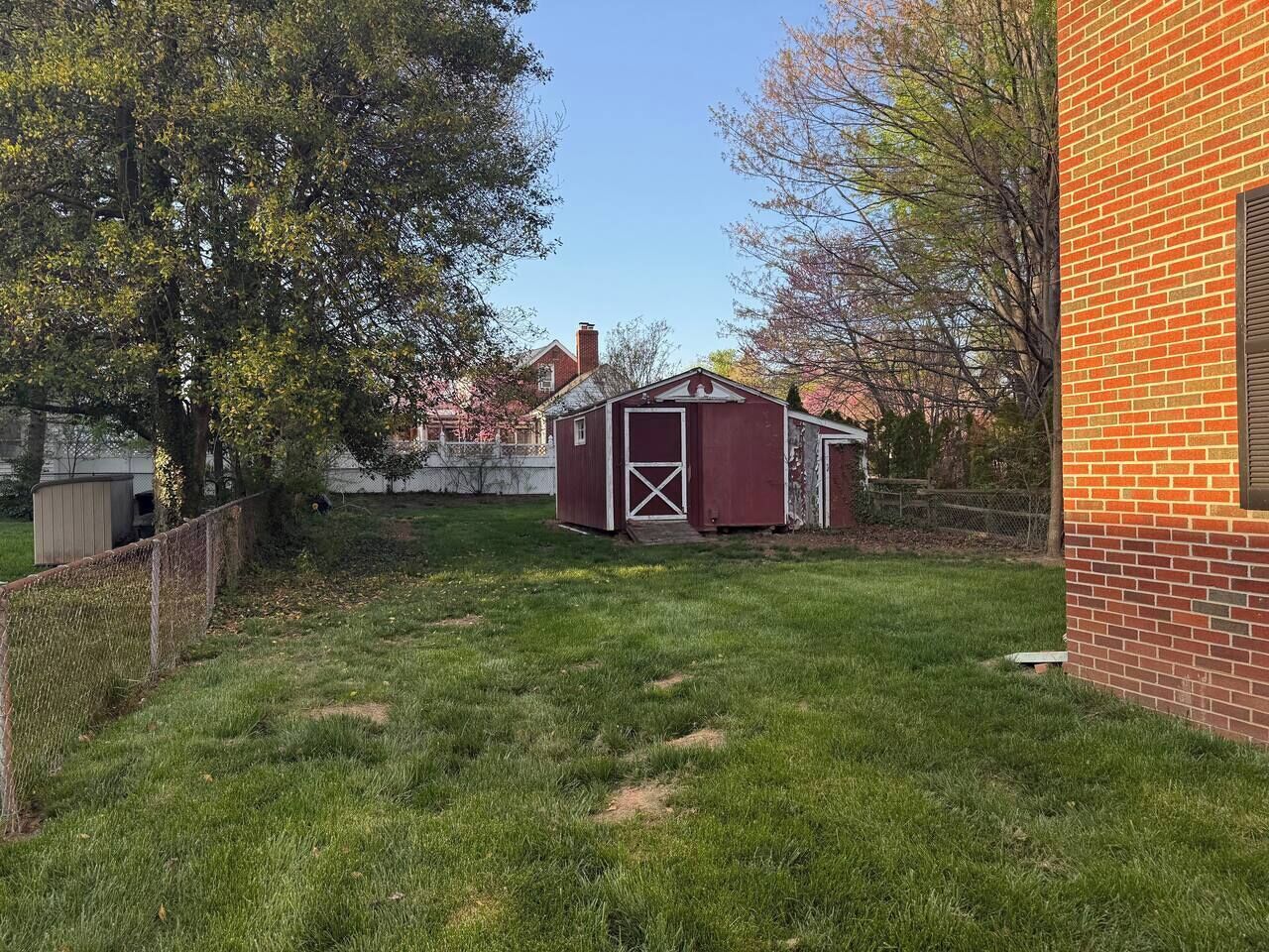 A backyard with a red shed, a brick wall, and a tree.