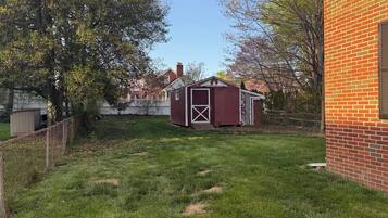 A backyard with a red shed, a brick wall, and a tree.