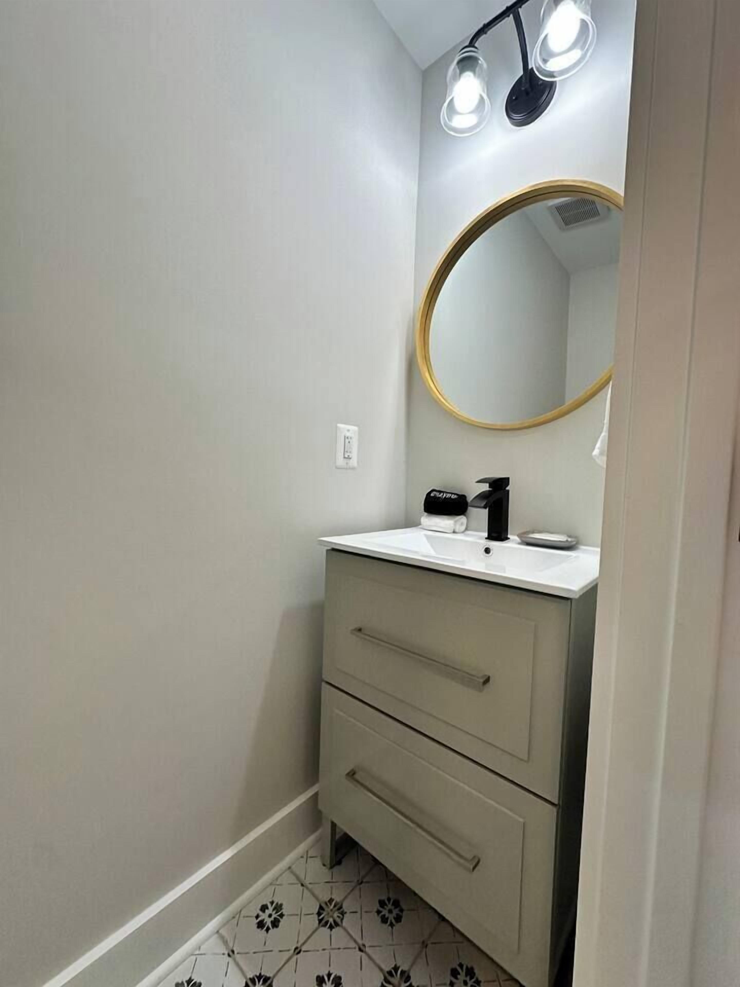 A bathroom with a white sink, a mirror with a gold frame, and a light fixture above the mirror.