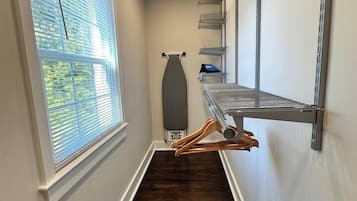Un pasillo estrecho con piso de madera, estanterías metálicas y una ventana con persianas.