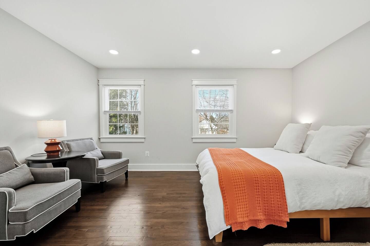 A bedroom with a bed, a sofa, a table, and two windows.