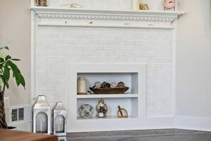 A white brick fireplace with decorative shelves above, a plant to the left, and a clock on the mantel.