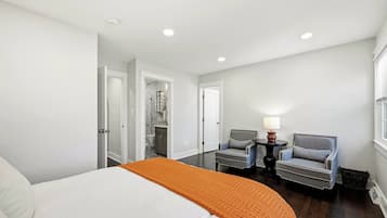 Une chambre d’hôtel avec un lit, deux fauteuils, une petite table avec une lampe et une salle de bain visible à travers une porte ouverte.