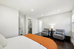 Habitación de hotel con cama, dos sillones, una mesita de noche con lámpara y un baño visible a través de una puerta abierta.